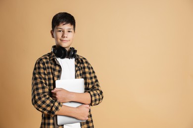 Photo of Portrait of teenage boy with laptop and headphones on beige background, space for text