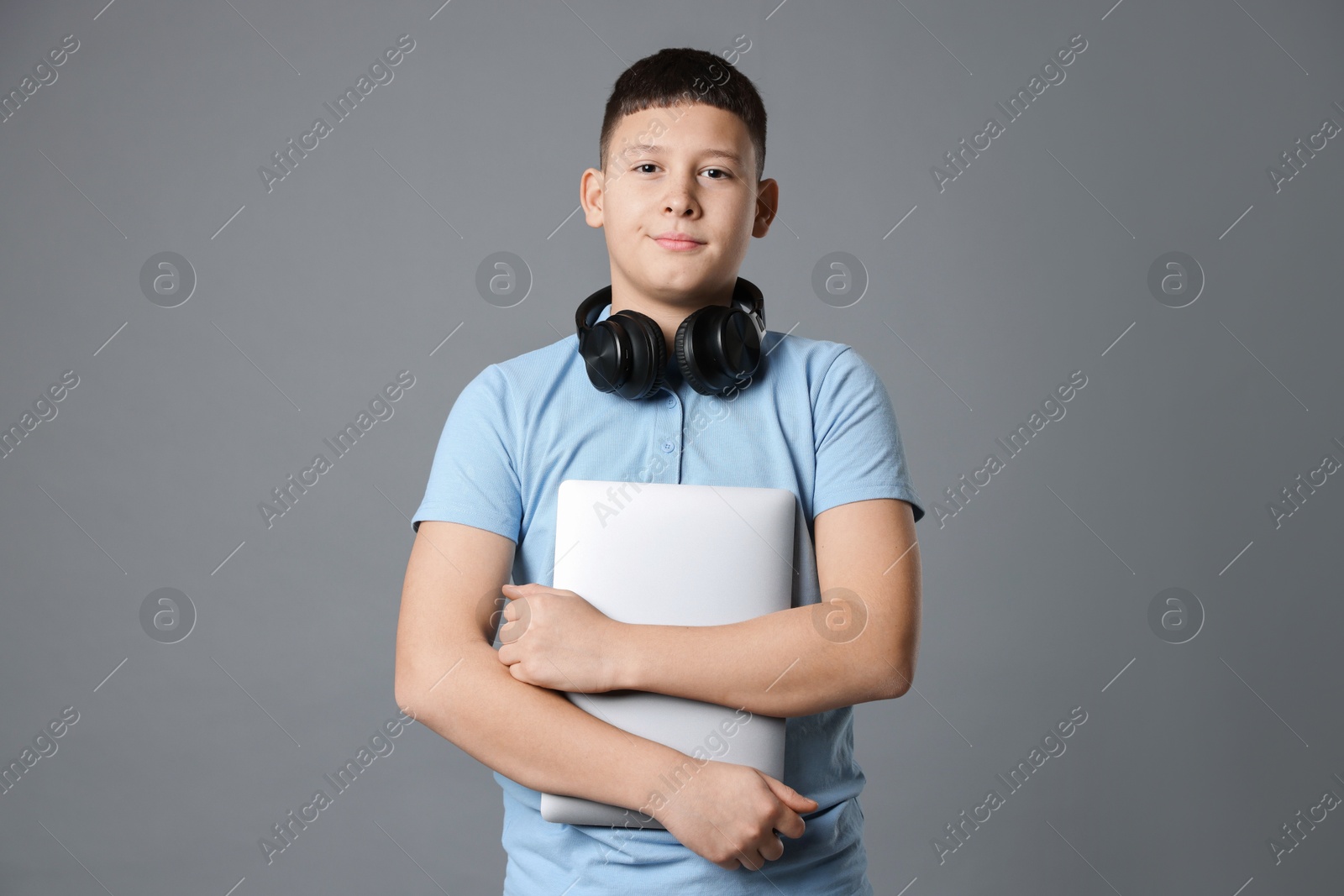 Photo of Portrait of teenage boy with laptop and headphones on grey background