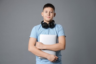 Photo of Portrait of teenage boy with laptop and headphones on grey background