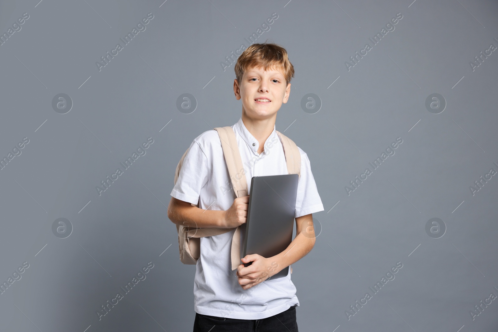 Photo of Portrait of teenage boy with laptop and backpack on grey background