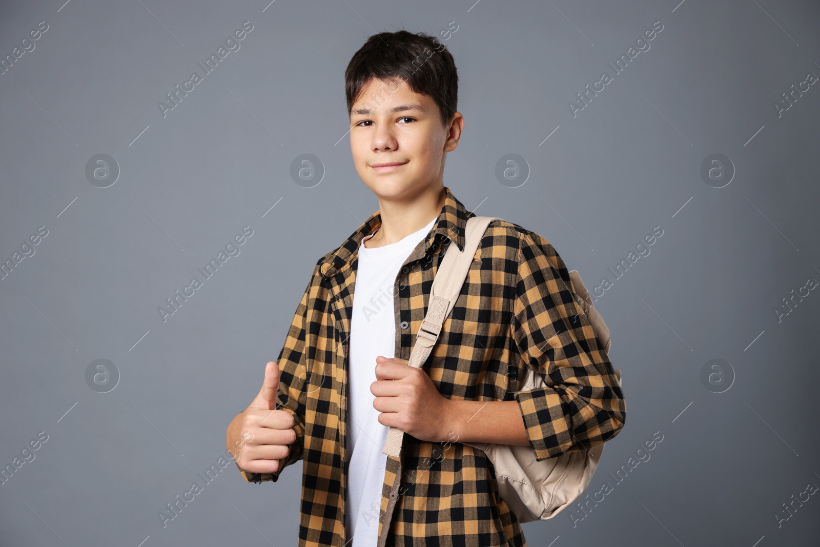 Photo of Portrait of teenage boy with backpack showing thumbs up on grey background