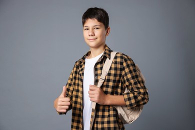 Photo of Portrait of teenage boy with backpack showing thumbs up on grey background