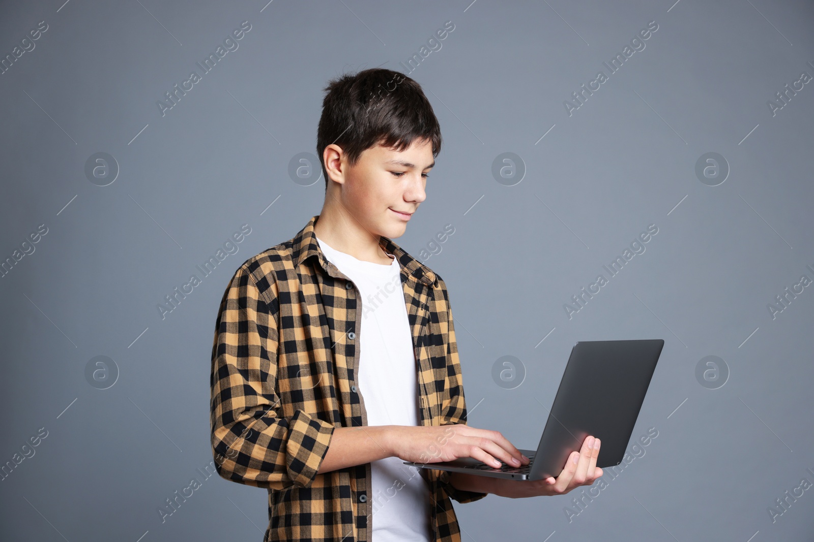 Photo of Portrait of teenage boy with laptop on grey background