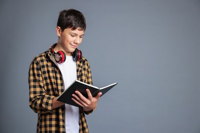 Photo of Portrait of teenage boy with book and headphones on grey background, space for text