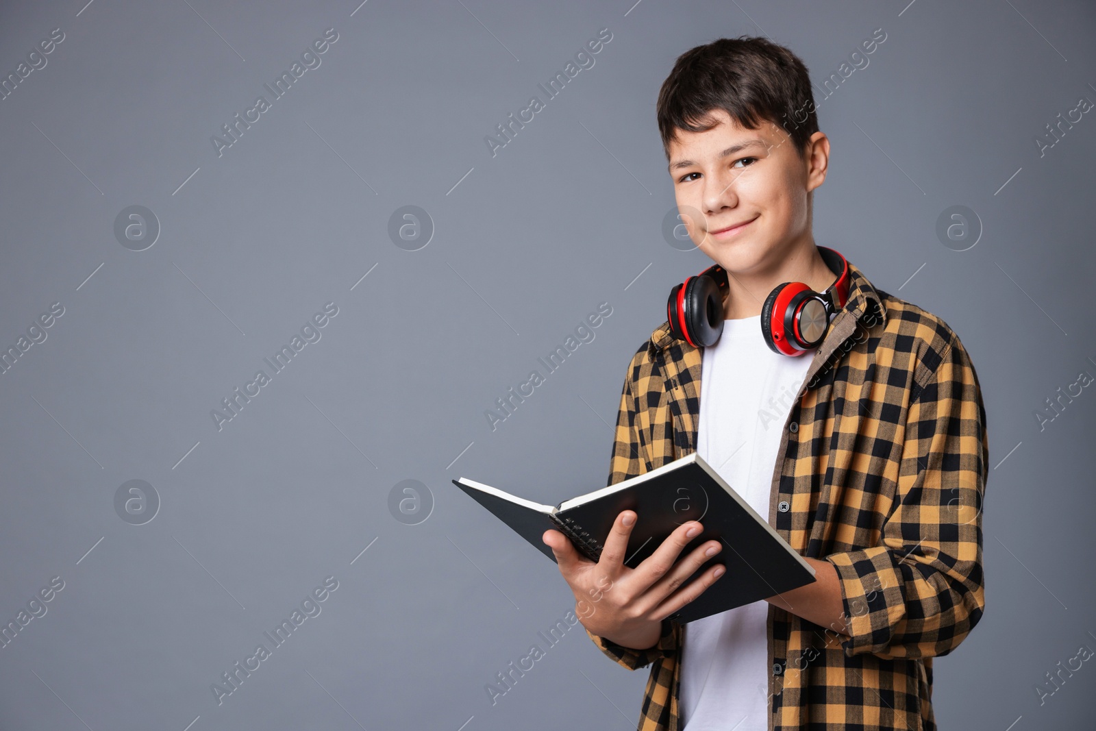 Photo of Portrait of teenage boy with book and headphones on grey background, space for text