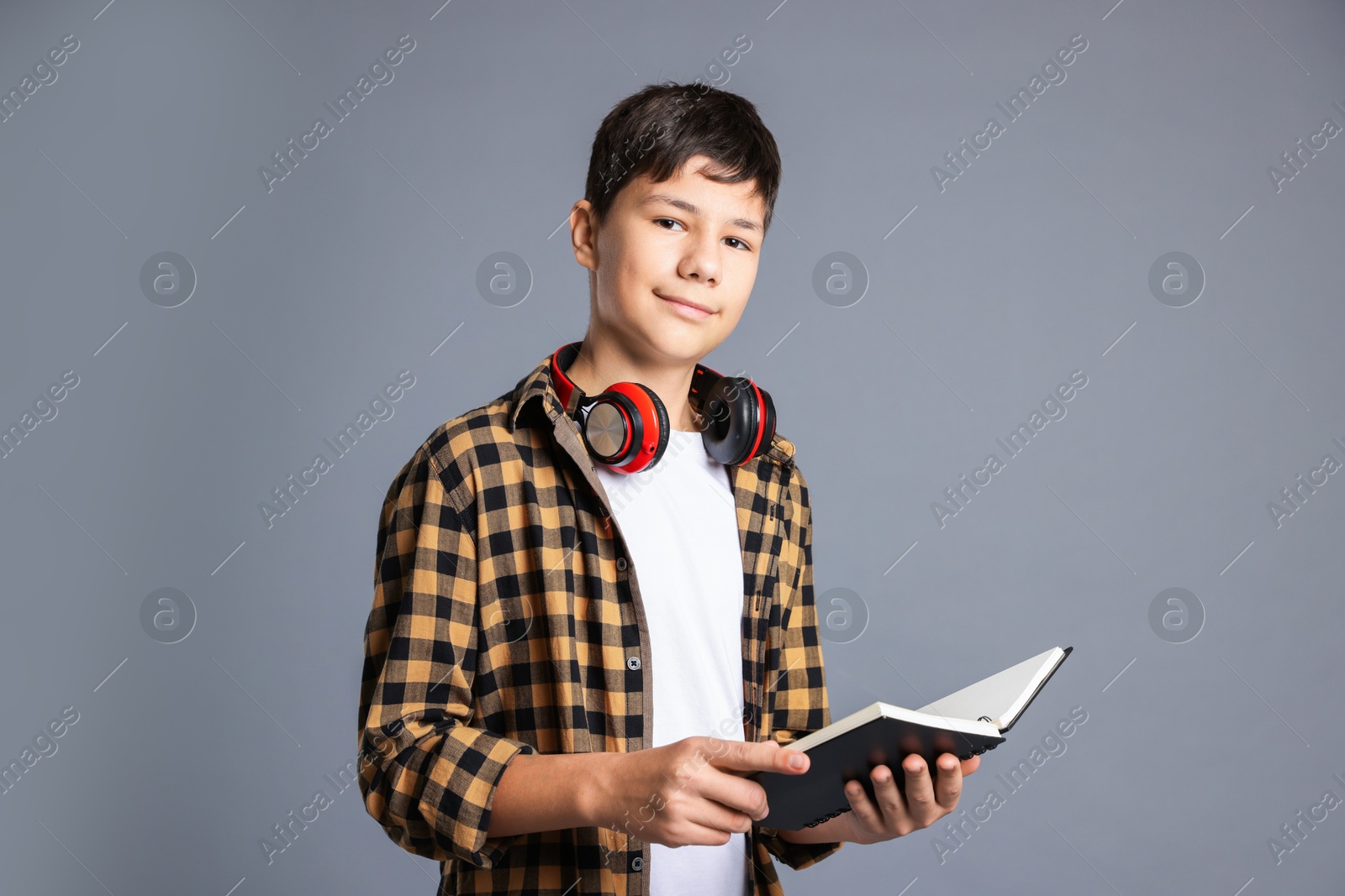 Photo of Portrait of teenage boy with book and headphones on grey background