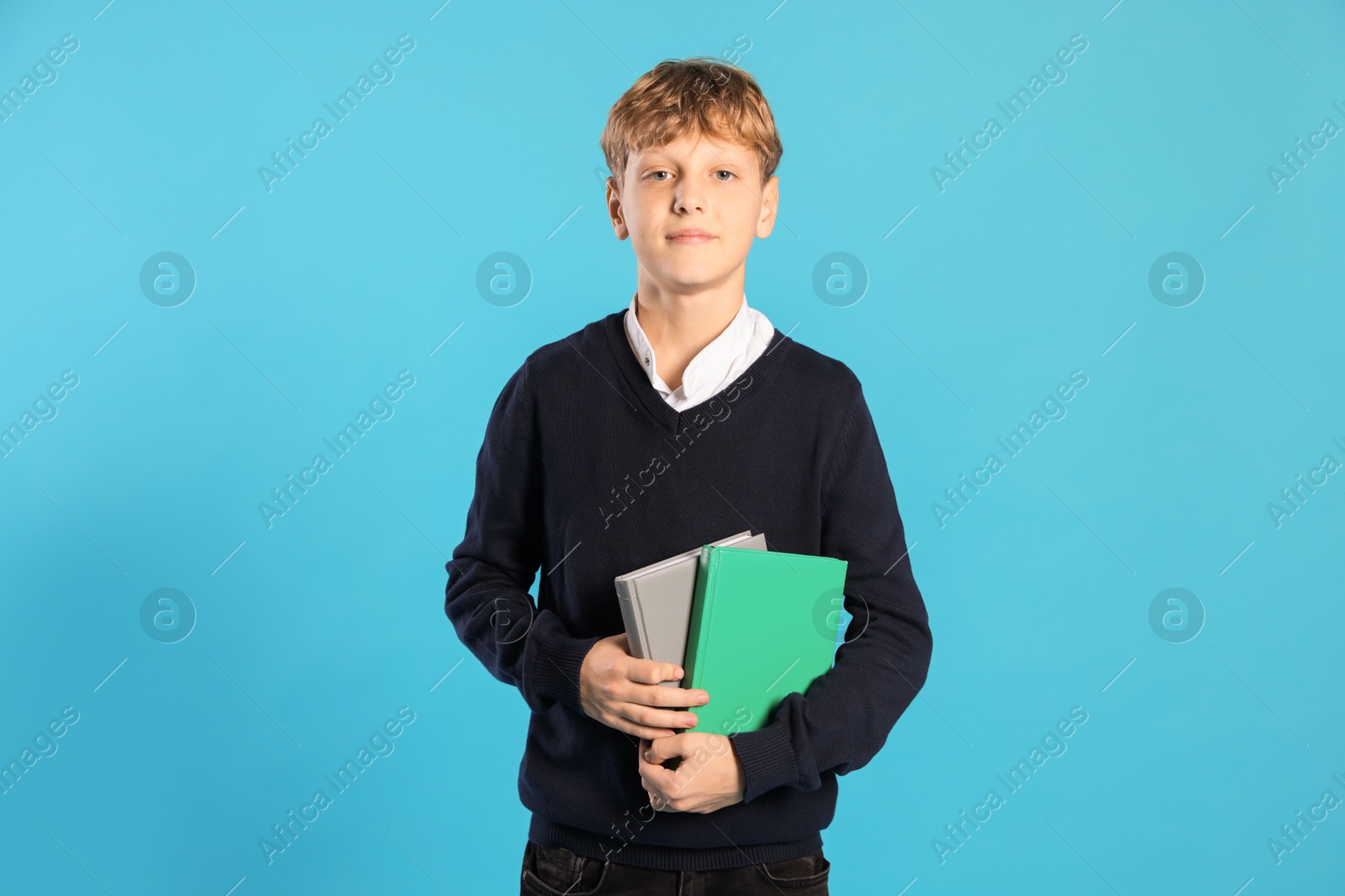 Photo of Portrait of teenage boy with books on light blue background