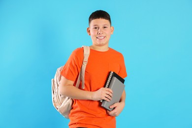 Photo of Portrait of teenage boy with books and backpack on light blue background