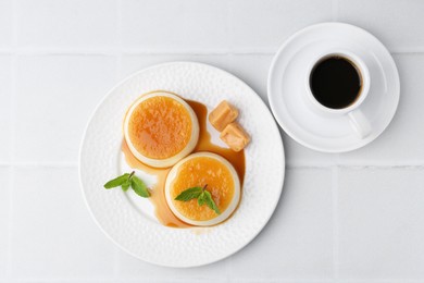 Photo of Tasty puddings with caramel sauce served on white tiled table, top view