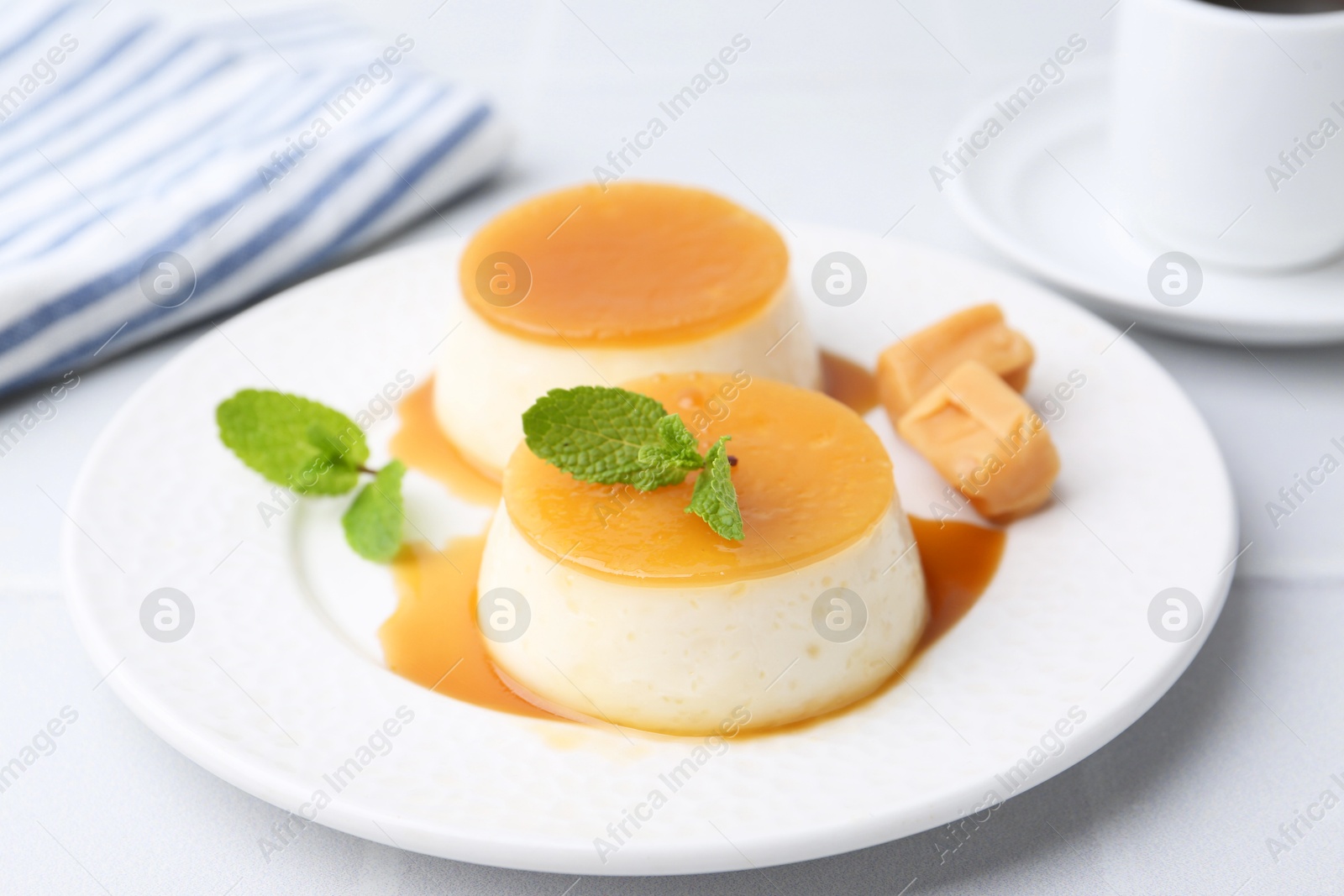 Photo of Tasty puddings with caramel sauce served on white tiled table, closeup