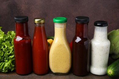 Photo of Tasty sauces in glass bottles and fresh products on wooden table, closeup