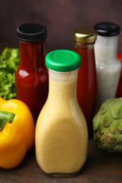 Photo of Tasty sauces in glass bottles and fresh products on wooden table, closeup