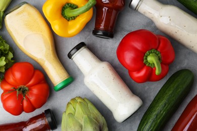 Photo of Tasty sauces in glass bottles and fresh products on light grey table, flat lay