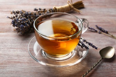 Aromatic lavender tea in glass cup, spoon and dry flowers on wooden table, closeup