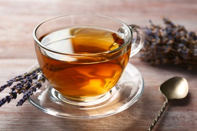 Photo of Aromatic lavender tea in glass cup, spoon and dry flowers on wooden table, closeup