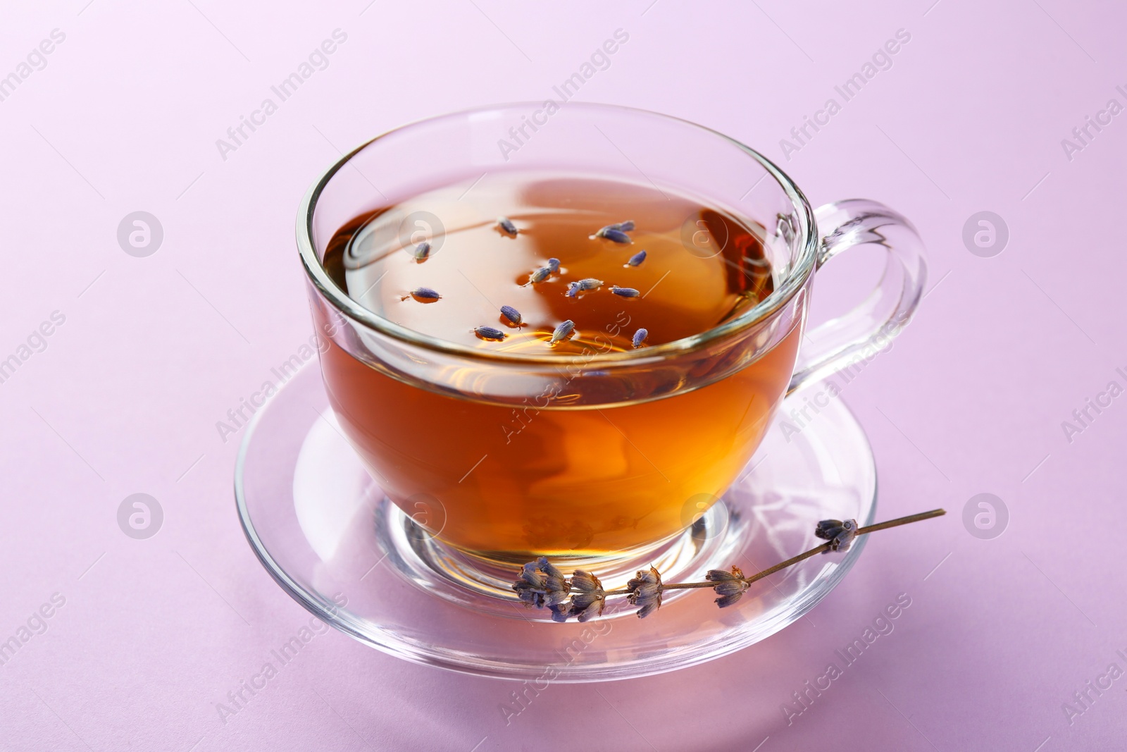 Photo of Aromatic lavender tea in glass cup and dry flower on pink background, closeup