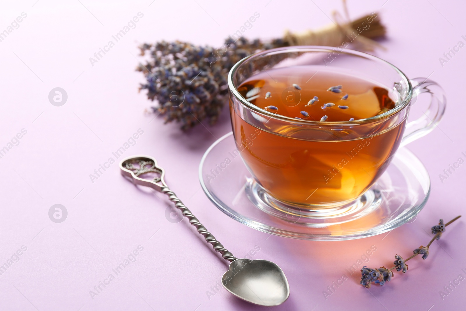 Aromatic lavender tea in glass cup, spoon and dry flowers on pink background, closeup. Space for text Photo of Aromatic lavender tea in glass cup, spoon and dry flowers on pink background, closeup. Space for text