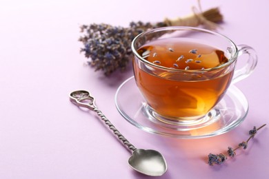 Photo of Aromatic lavender tea in glass cup, spoon and dry flowers on pink background, closeup. Space for text