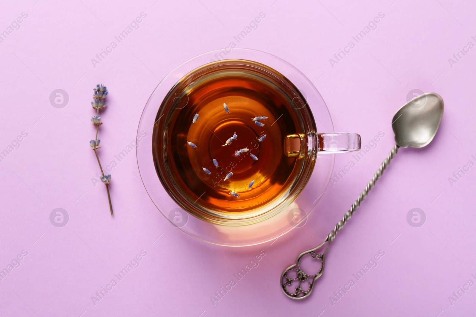 Aromatic lavender tea in glass cup, spoon and dry flower on pink background, top view Photo of Aromatic lavender tea in glass cup, spoon and dry flower on pink background, top view