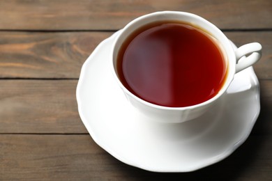 Photo of Refreshing black tea in cup on wooden table, closeup