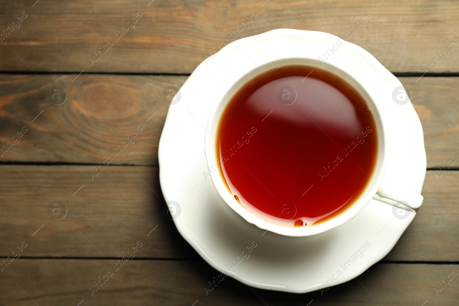 Photo of Refreshing black tea in cup on wooden table, top view. Space for text