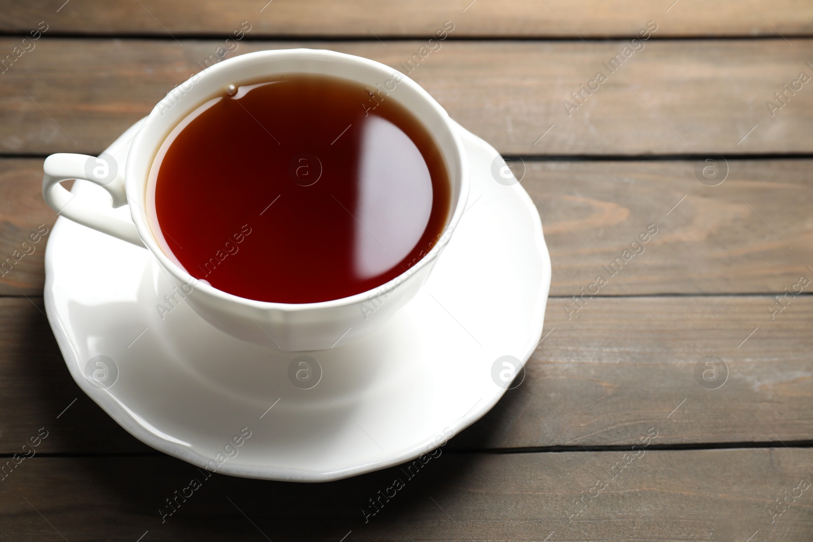 Photo of Refreshing black tea in cup on wooden table, closeup. Space for text