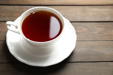 Refreshing black tea in cup on wooden table, closeup. Space for text