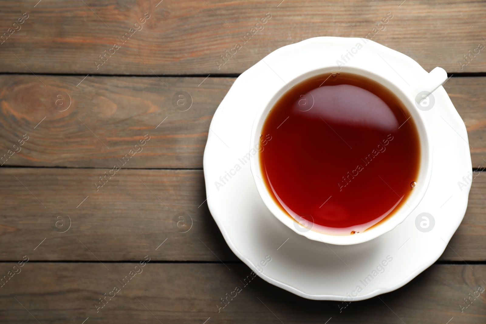 Photo of Refreshing black tea in cup on wooden table, top view. Space for text