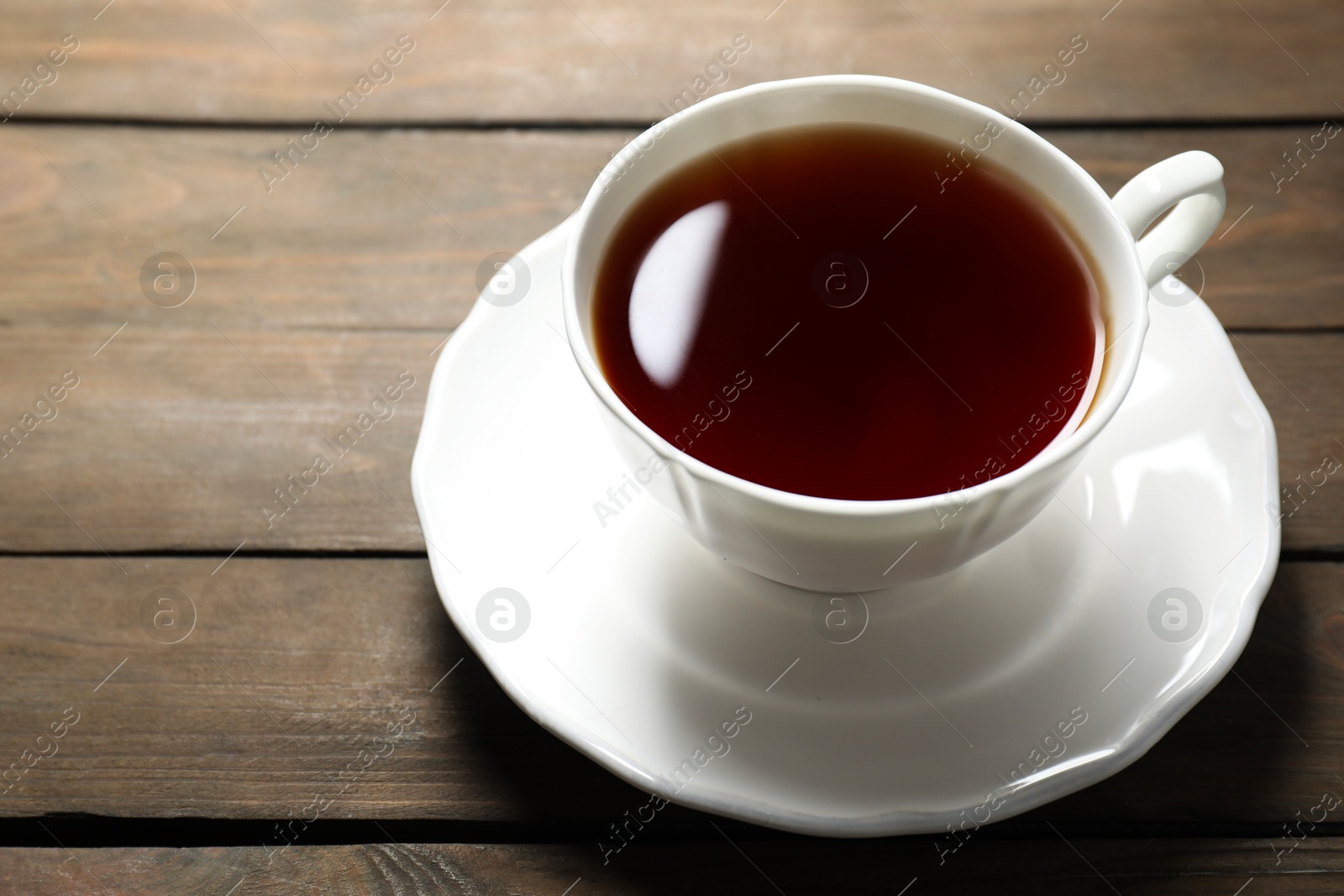 Photo of Refreshing black tea in cup on wooden table, closeup. Space for text