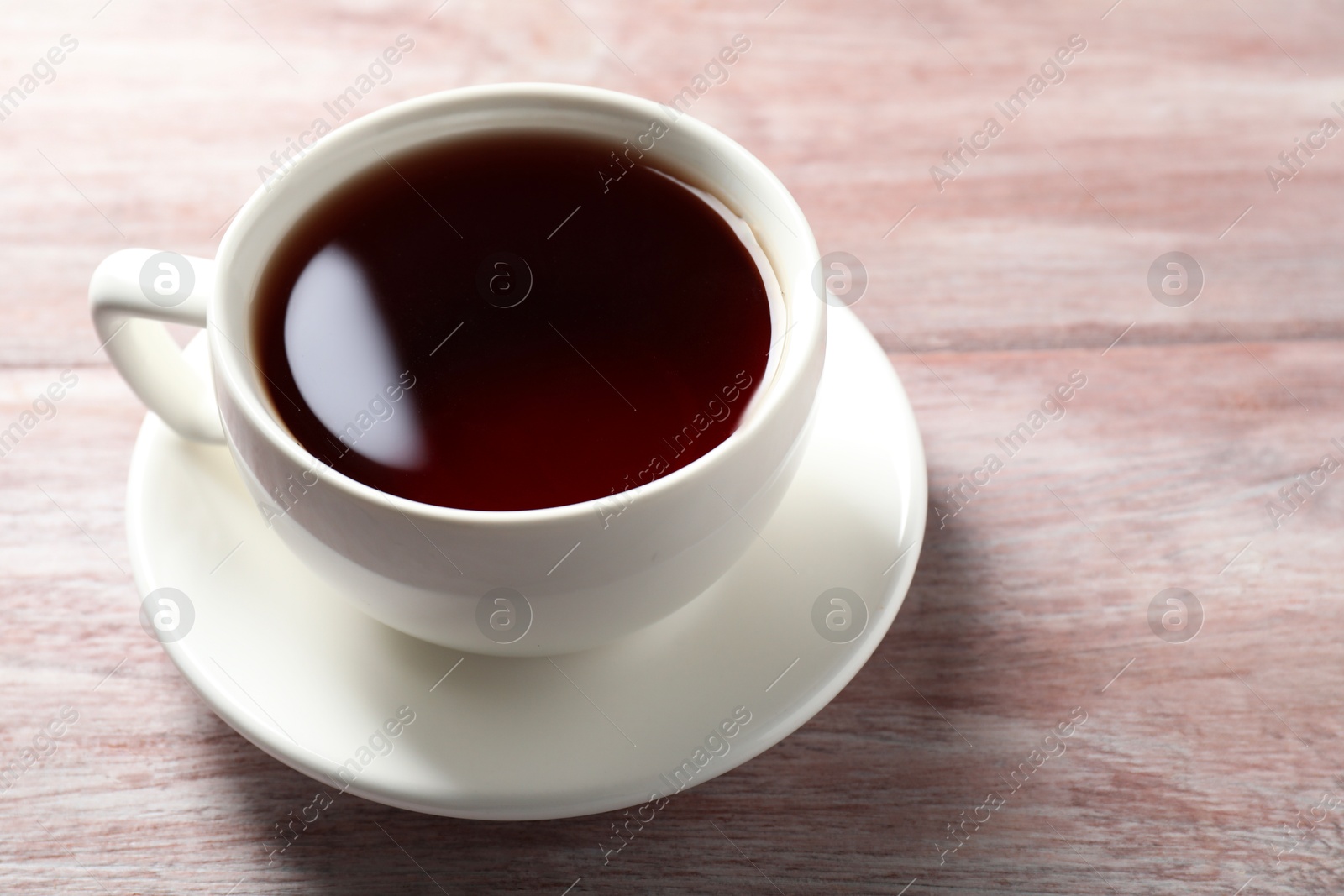 Photo of Refreshing black tea in cup on light wooden table, closeup. Space for text