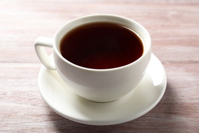 Photo of Refreshing black tea in cup on light wooden table, closeup