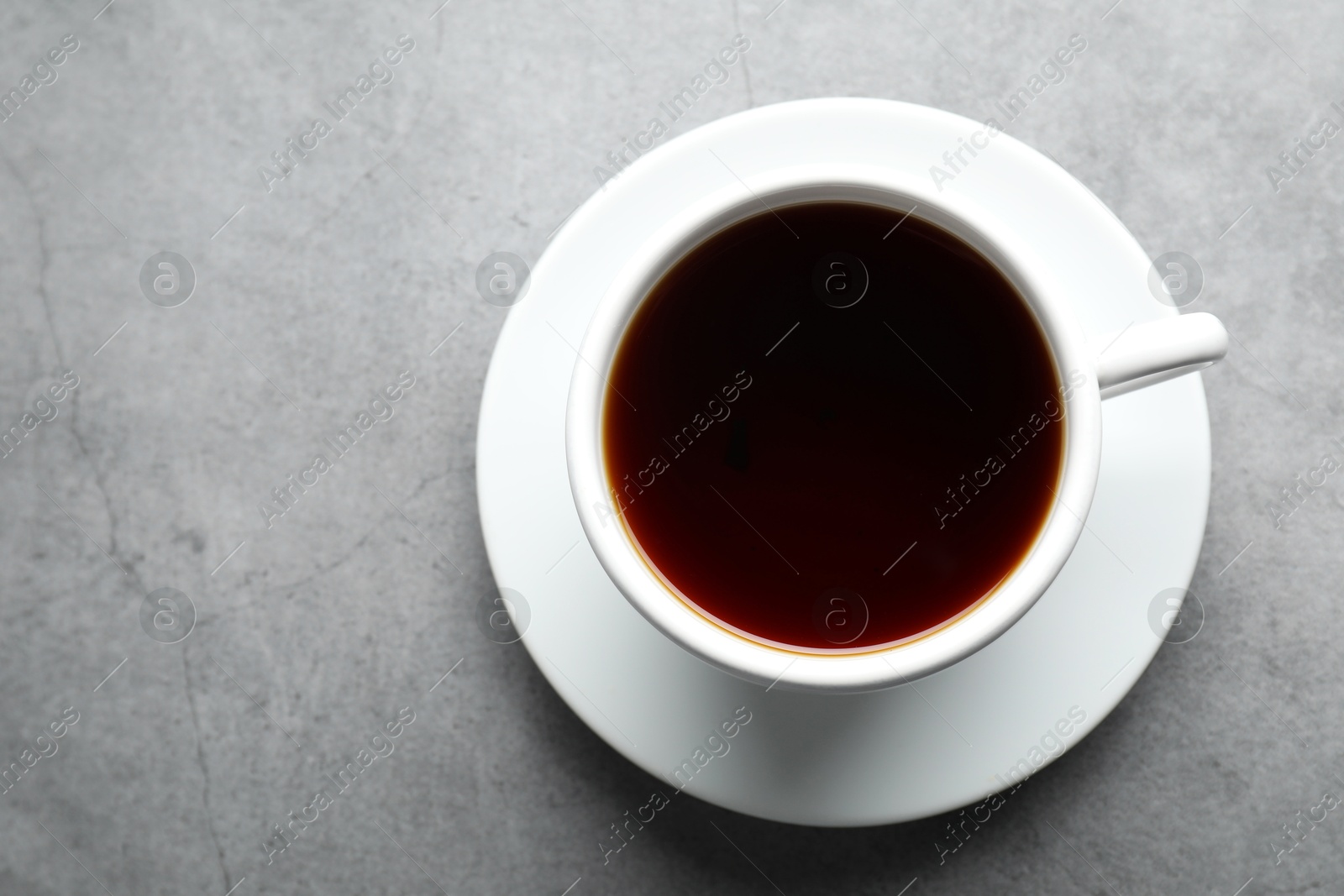 Photo of Refreshing black tea in cup on grey textured table, top view. Space for text