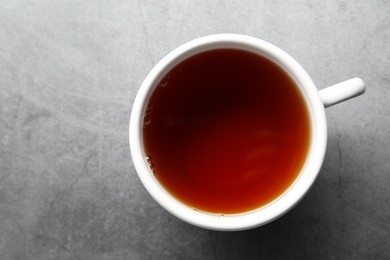 Photo of Refreshing black tea in cup on grey textured table, top view. Space for text