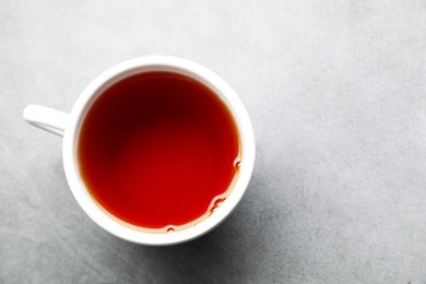 Photo of Refreshing black tea in cup on grey textured table, top view. Space for text