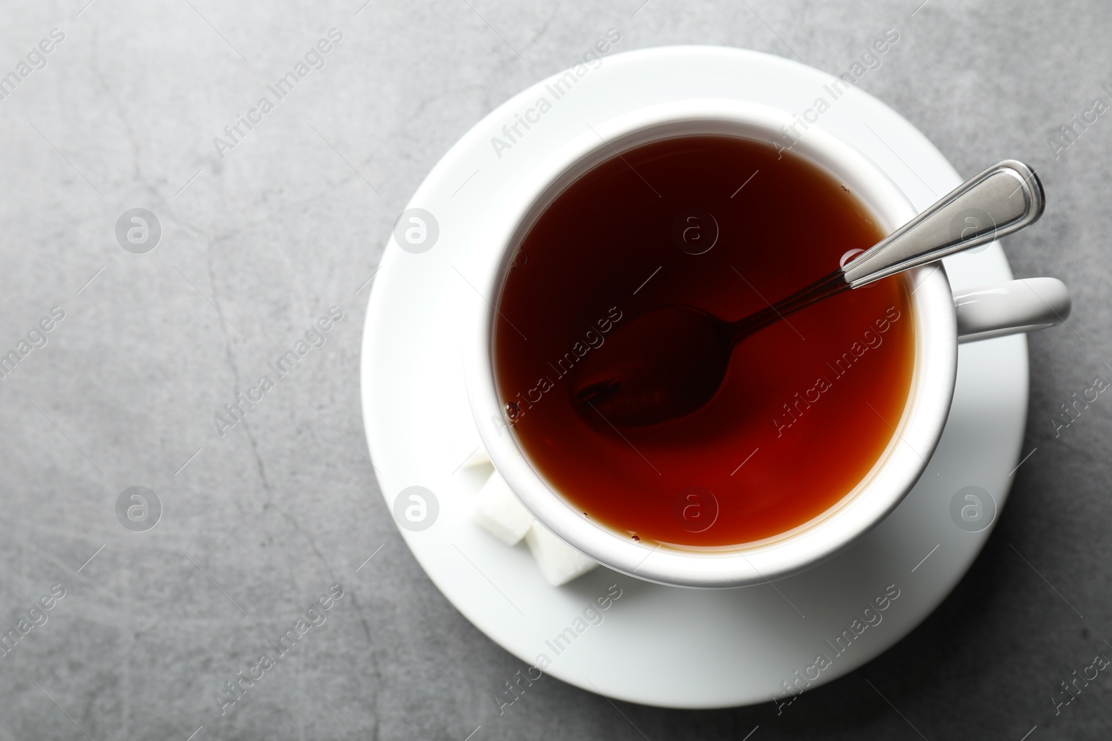 Photo of Refreshing black tea in cup and sugar cubes on grey textured table, top view. Space for text