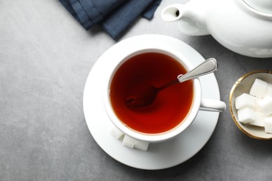 Photo of Refreshing black tea in cup, sugar cubes and teapot on grey textured table, flat lay. Space for text