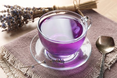 Photo of Aromatic lavender tea in glass cup, spoon and bunch of dry flowers on table, closeup