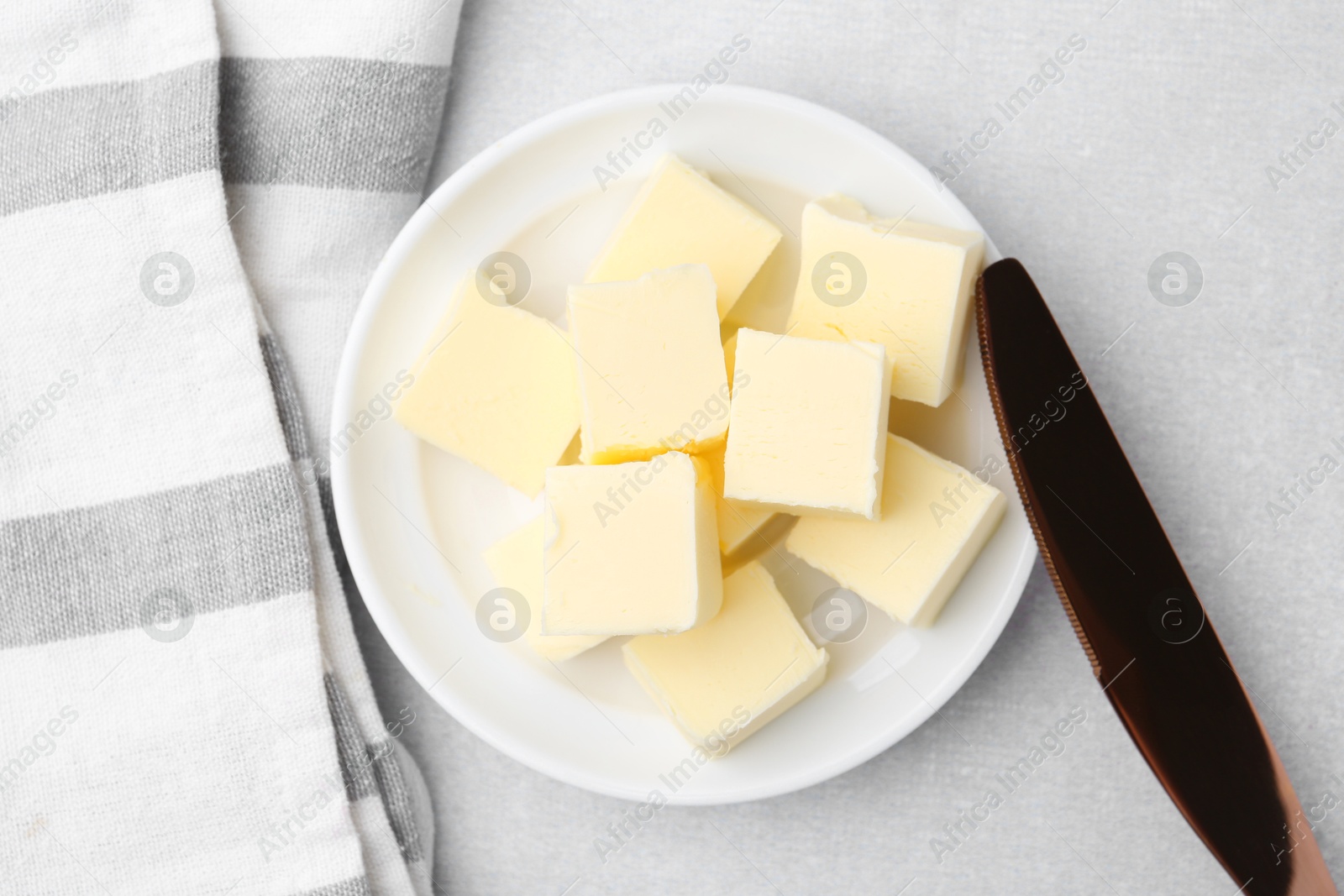 Photo of Pieces of fresh butter and knife on white table, top view