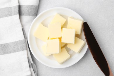 Photo of Pieces of fresh butter and knife on white table, top view