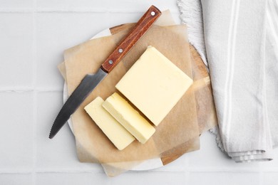 Photo of Cut block of fresh butter and knife on white tiled table, top view