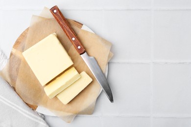 Cut block of fresh butter and knife on white tiled table, top view. Space for text