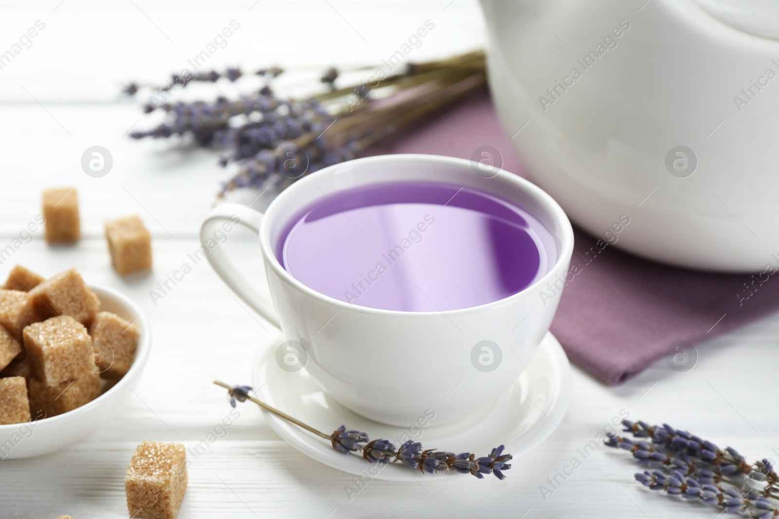 Aromatic lavender tea in cup, brown sugar and dry flowers on white wooden table, closeup Photo of Aromatic lavender tea in cup, brown sugar and dry flowers on white wooden table, closeup