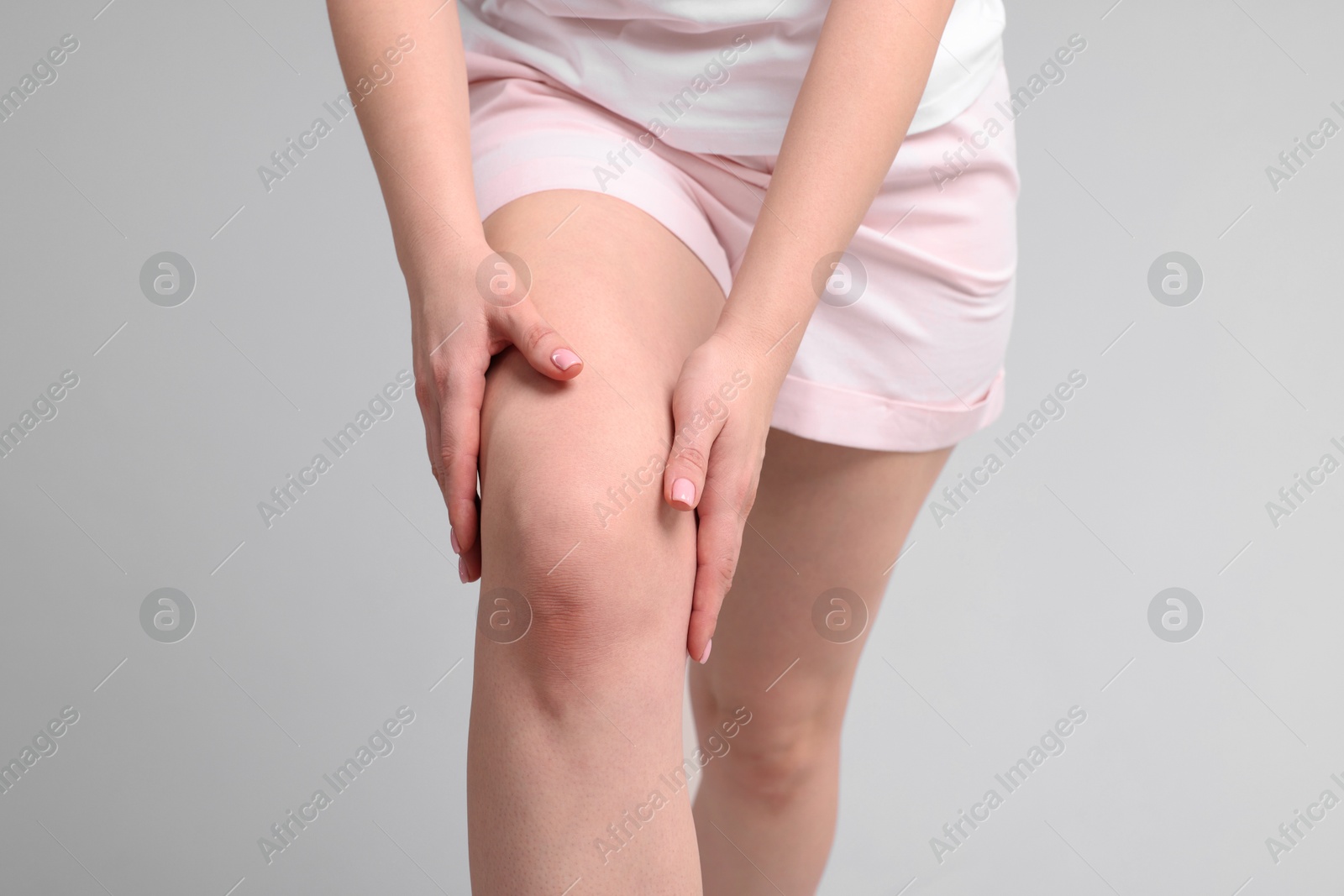 Photo of Young woman suffering from pain in knee on light grey background, closeup