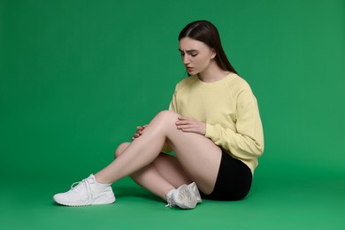 Photo of Young woman suffering from pain in knee on green background