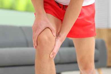 Photo of Young man suffering from pain in knee at home, closeup