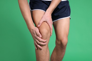 Photo of Young man suffering from pain in knee on green background, closeup