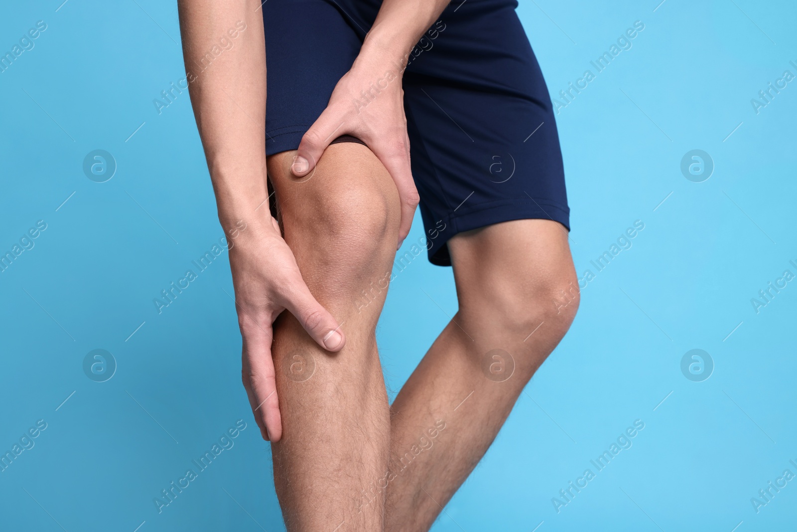 Photo of Young man suffering from pain in knee on light blue background, closeup