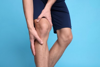 Photo of Young man suffering from pain in knee on light blue background, closeup