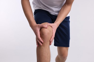 Photo of Young man suffering from pain in knee on light grey background, closeup