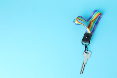 Photo of Key with keychain in LGBT colors on light blue background, top view. Space for text